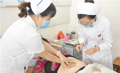 图为该科护士长和护士正在根据患者手指关节长度准确定位敷贴穴位